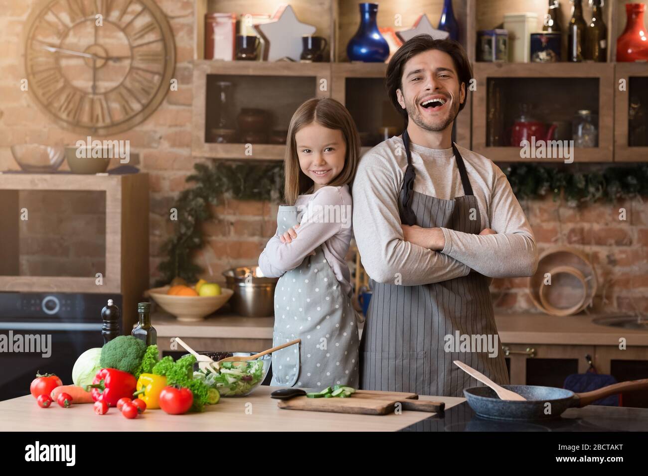 Padre e figlia condifent in grembiuli che posano sullo sfondo della cucina Foto Stock