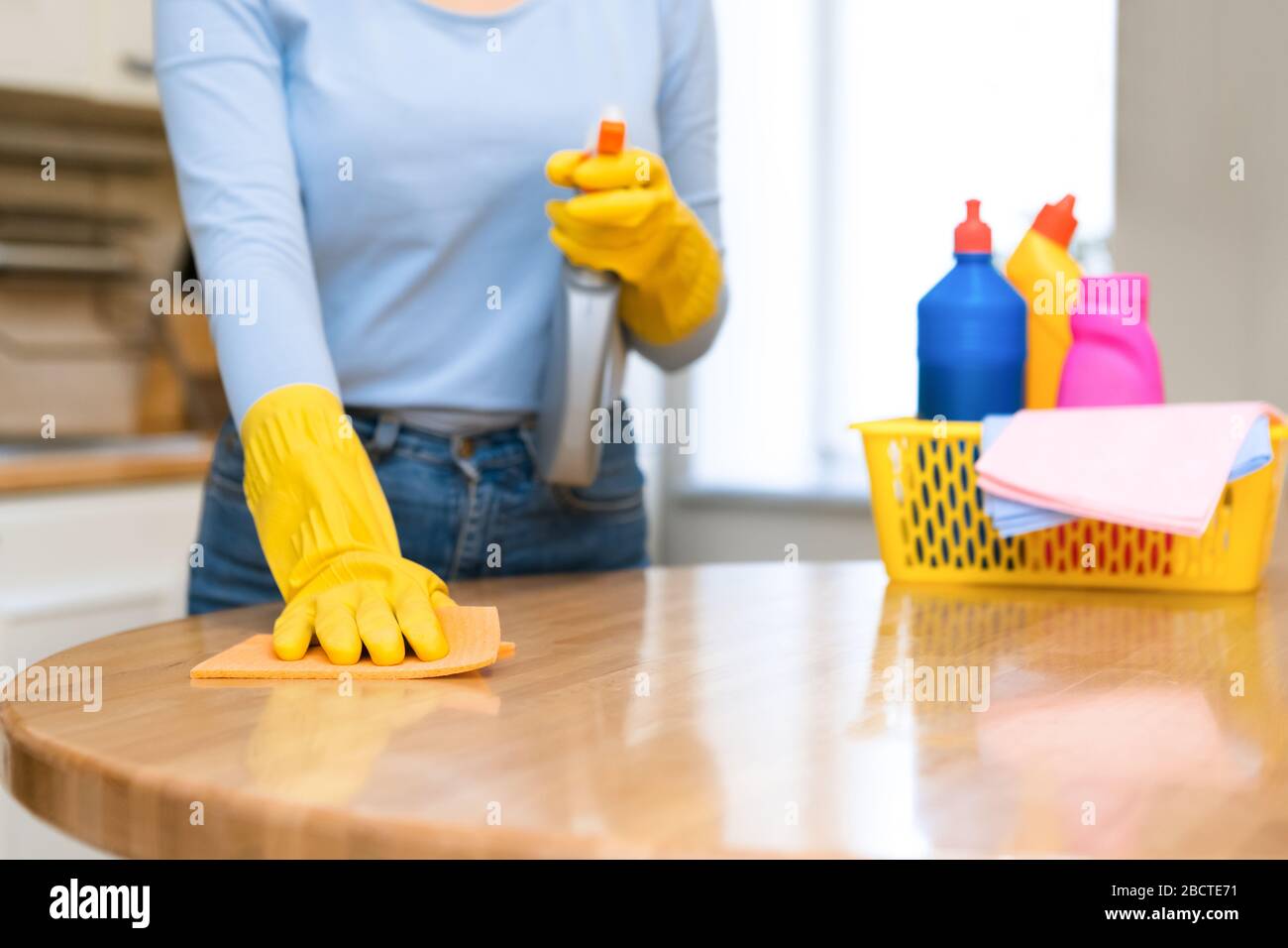 Giovane donna pulizia tavolo da cucina con spray e straccio Foto Stock