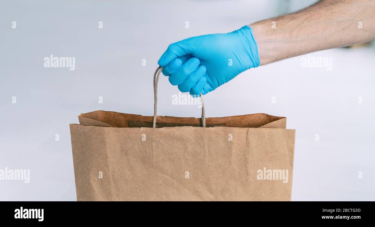Negozio di alimentari consegna negozio uomo che dà sacchetto di carta indossando guanto blu come protezione per COVID-19 Coronavirus precauzioni. Foto Stock