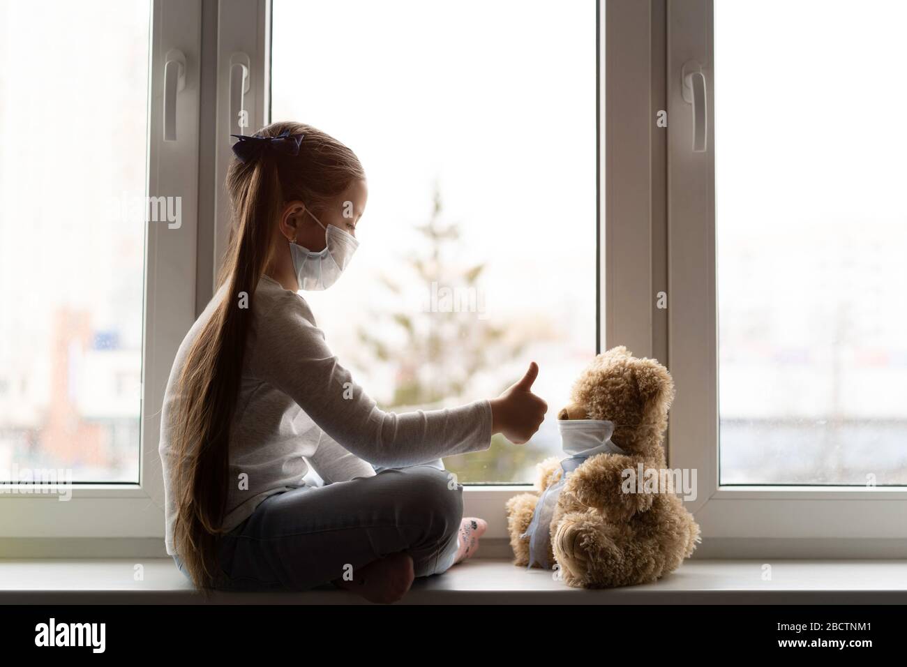 Triste bambino e il suo orso di teddy entrambi in maschere mediche protettive. Bambini e malattie COVID-2019 concetto di malattia Foto Stock