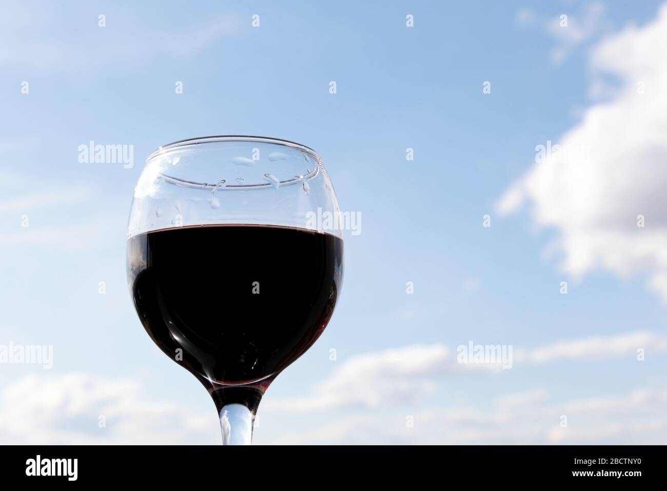 Bicchiere di vino rosso sullo sfondo del cielo blu con nuvole bianche. Concetto di festa, festa in casa, cena romantica all'aperto Foto Stock