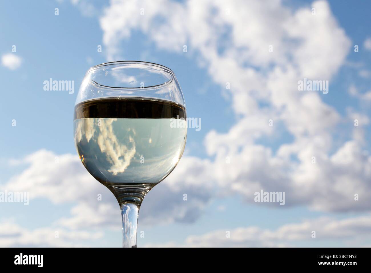 Bicchiere di vino bianco sullo sfondo del cielo blu, le nuvole si riflettono nella bevanda alcolica. Concetto di festa, festa in casa, cena romantica all'aperto Foto Stock