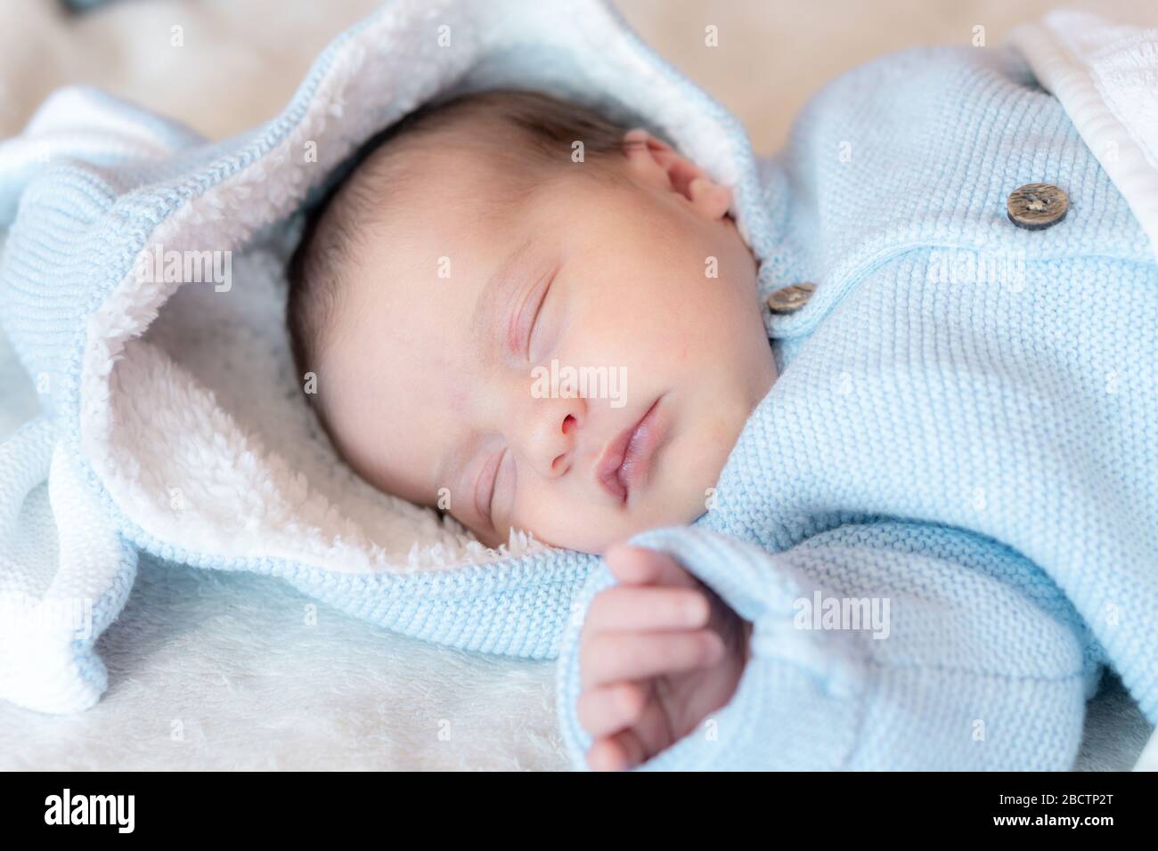 Primo piano sul neonato. Vista laterale di un neonato che dorme saldamente sulla schiena in una blusa blu con cappuccio e orecchie su sfondo bianco. Verticale Foto Stock