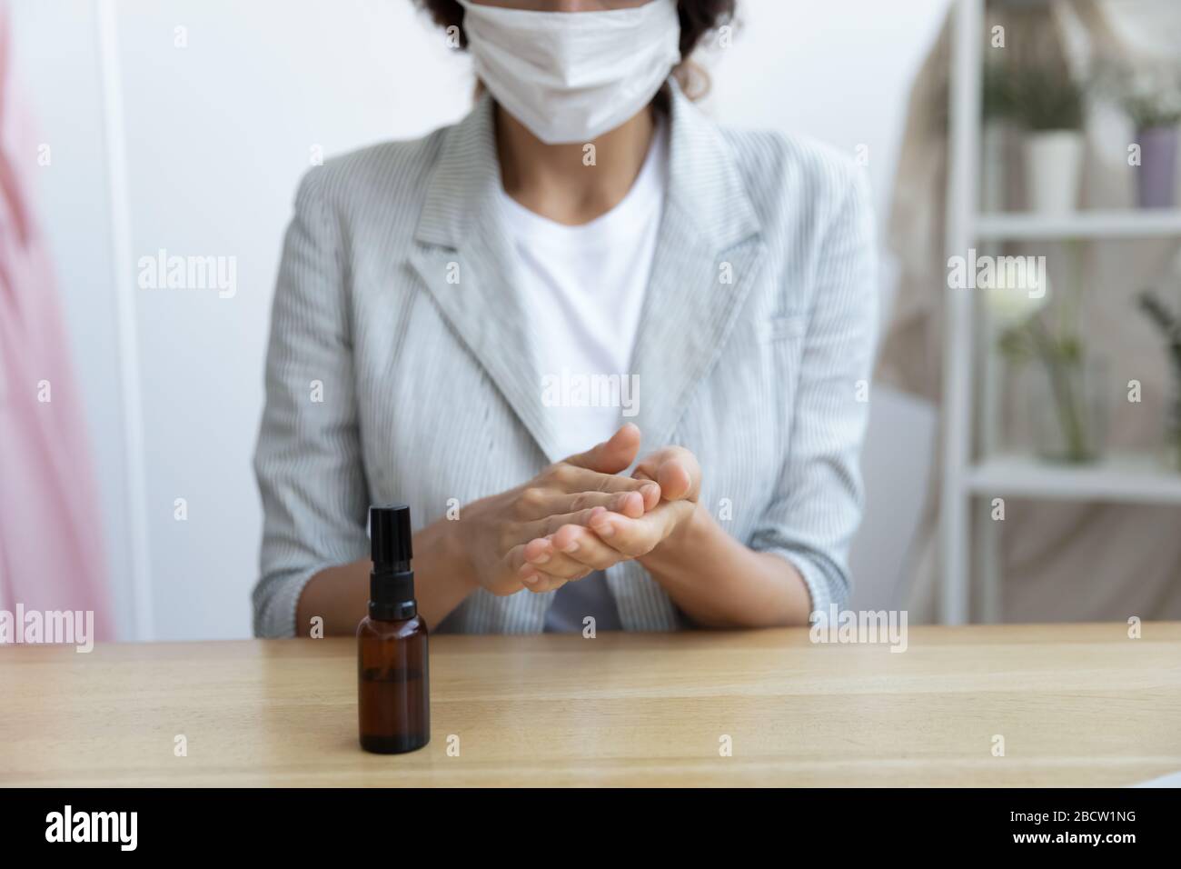 Donna d'affari in maschera viso igienizzante mani con spray. Foto Stock