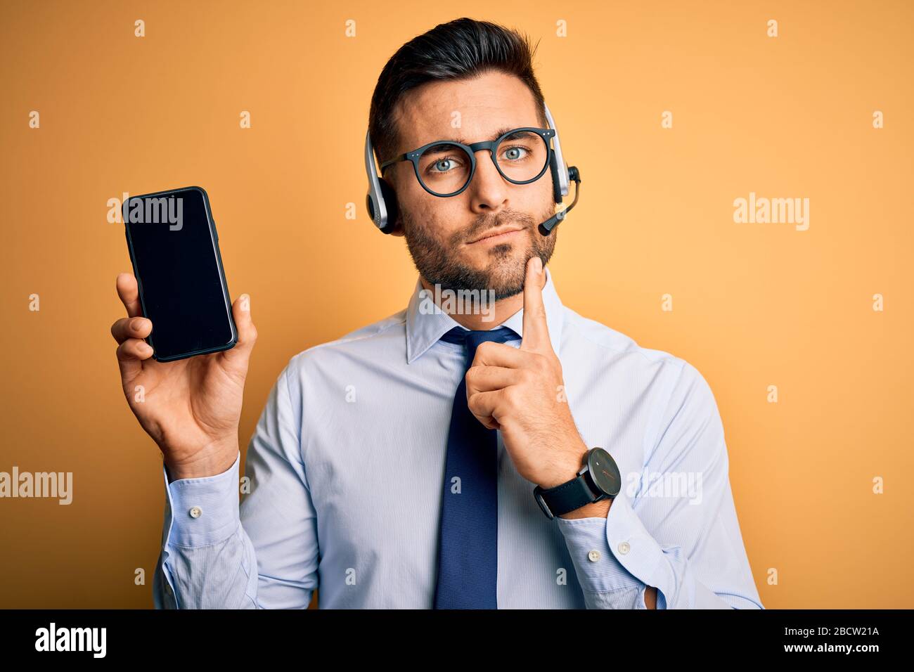 Operatore aziendale con cuffia per il servizio clienti del call center che mostra lo schermo dello smartphone faccia seria pensare alla domanda, ide molto confuso Foto Stock