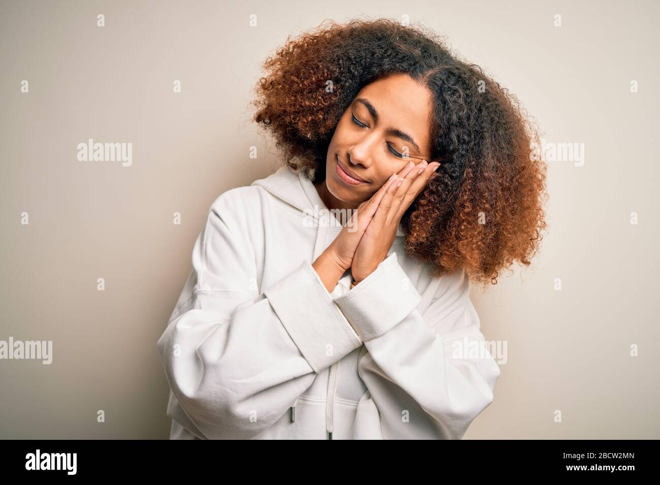 Giovane sportswoman afroamericana con capelli afro indossando felpa sportiva dormire stanco sognare e posare con le mani insieme sorridendo con Foto Stock