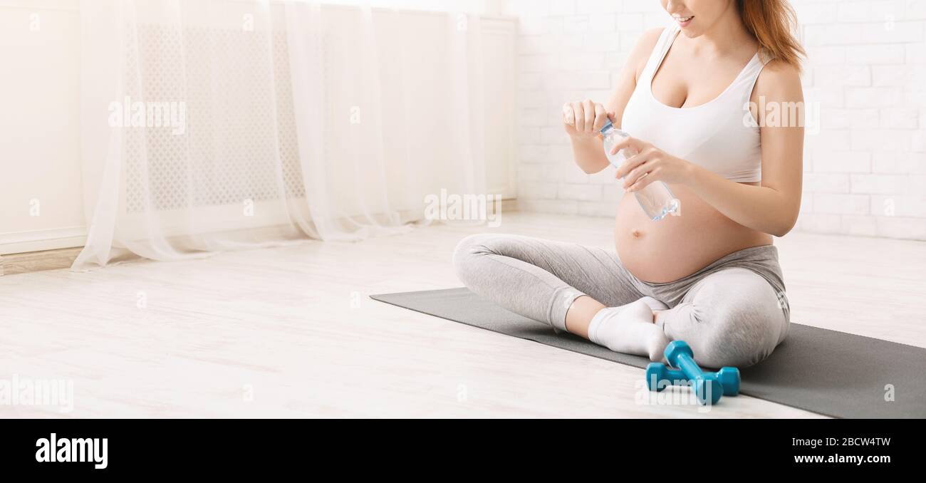 Giovane donna incinta che beve acqua seduta in posizione lotus Foto Stock