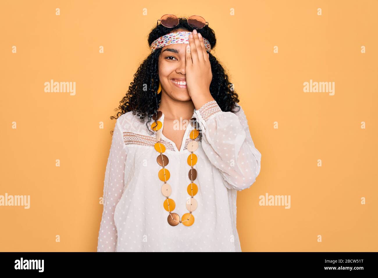 Giovane afro americano malata hippie donna indossando occhiali da sole e  accessori vintage coprendo un occhio con la mano, sorriso sicuro sul viso e  sorpresa Foto stock - Alamy