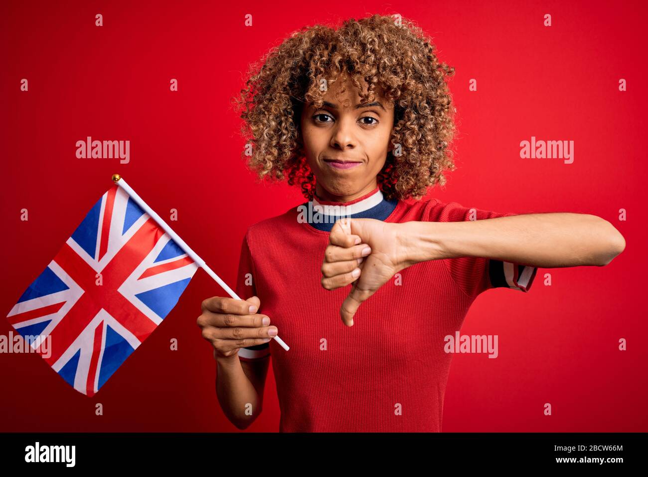 Giovane donna maledetta afroamericana che tiene la bandiera britannica per celebrare il referendum sulla brexit con il volto arrabbiato, segno negativo che mostra antipatia con i pollici giù, reje Foto Stock