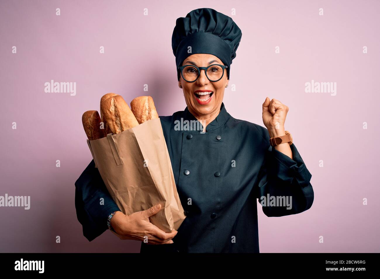 Donna panettiere di media età che indossa l'uniforme del fornello e cappello  che tiene la borsa di carta con il pane che urla fiero e che celebra la  vittoria ed il successo