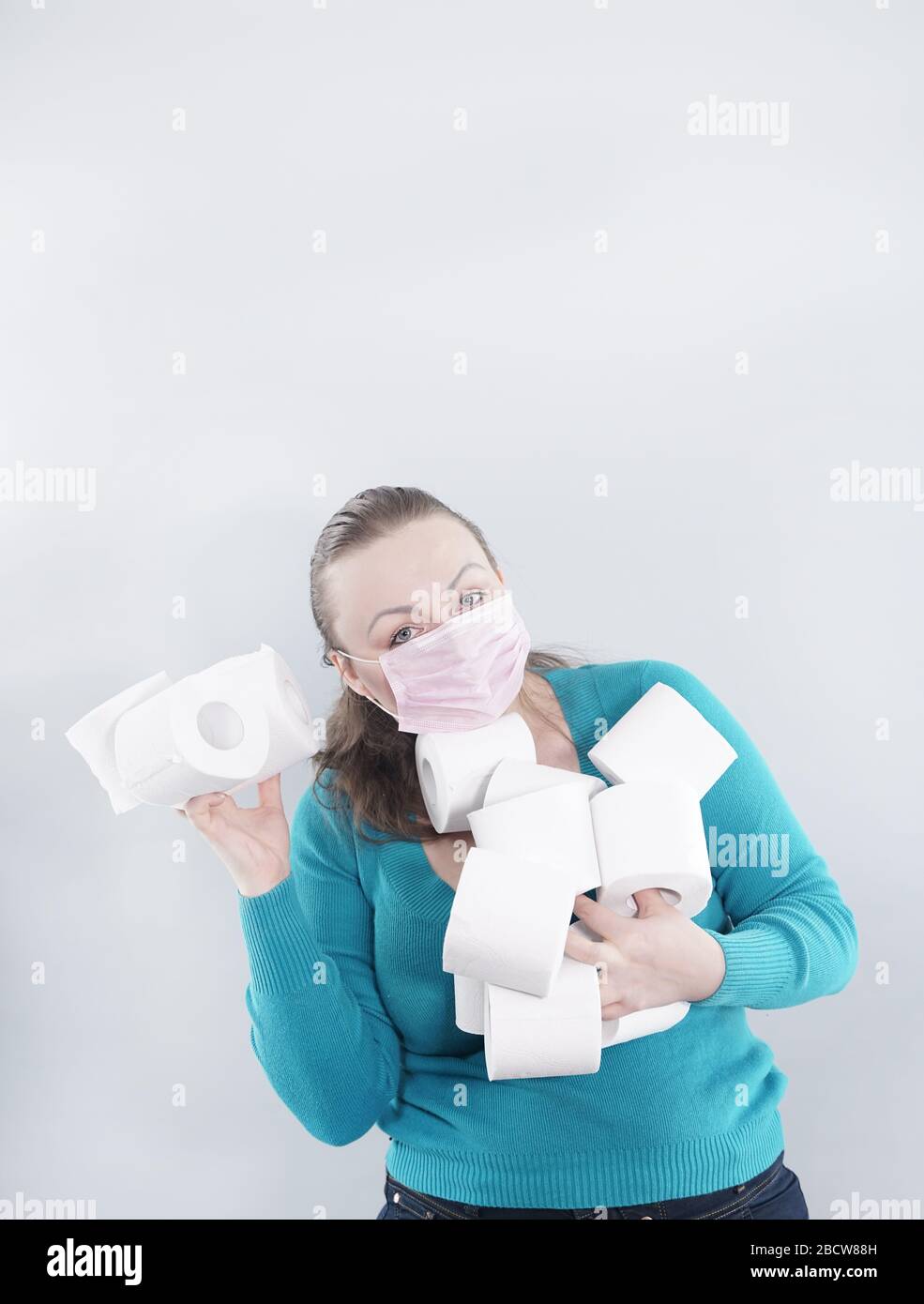 Una donna indossa una maschera facciale per la protezione dal virus Corona e si è rifornita di carta igienica in caso di quarantena. FEM di mezza età Foto Stock