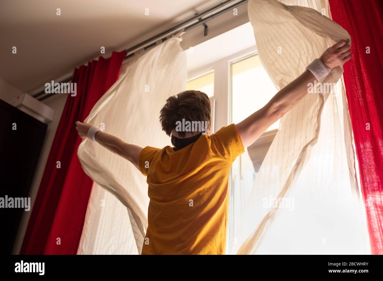 Uomo caucasico che apre le tende sulla finestra alla luce del mattino Foto Stock