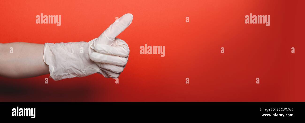 Mano del bambino nel guanto medico grande mostra il pollice su su sfondo rosso, posto per il testo, formato della bandiera Foto Stock