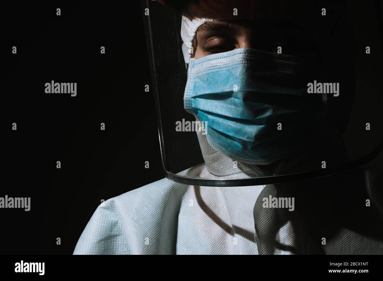 Medico femmina triste e grave con maschera e schermo per la protezione del coronavirus covid-19 su sfondo nero Foto Stock