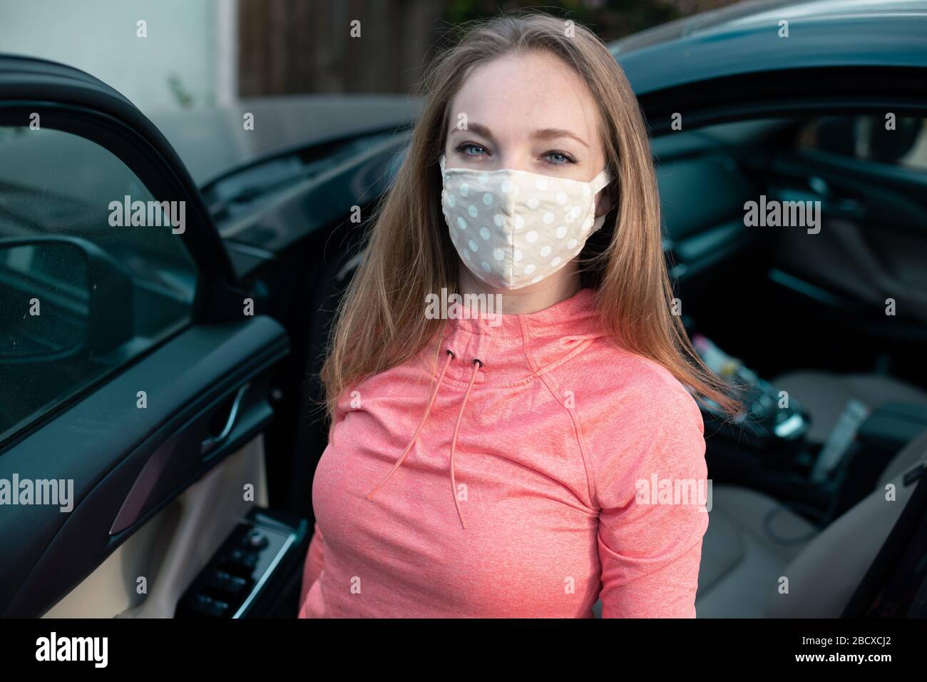 Giovane donna in tessuto maschera viso accanto alla sua auto. Molti paesi raccomandano ai cittadini di coprire il loro volto durante la pandemia di coronavirus mondiale. Foto Stock