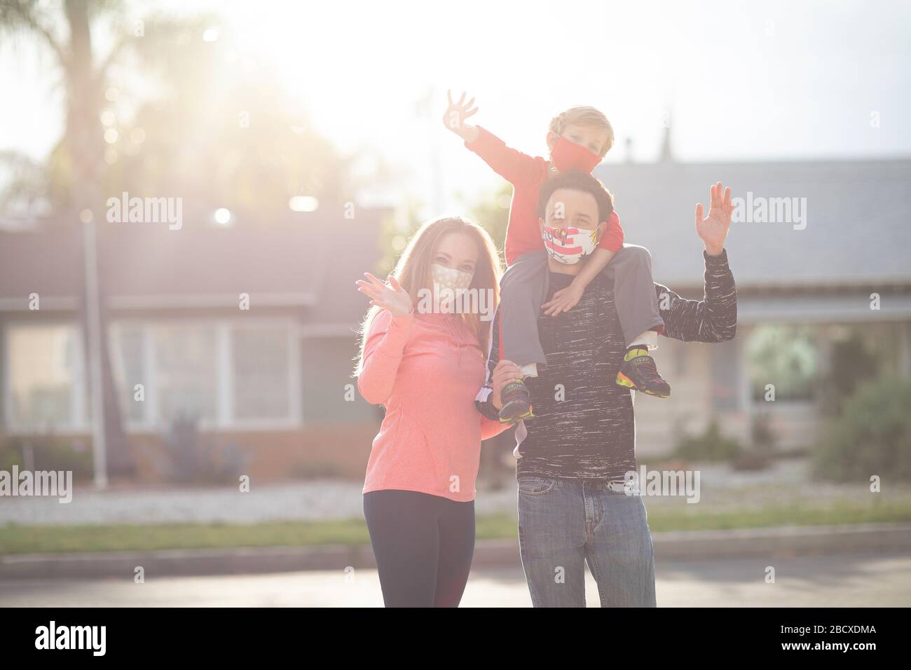 La famiglia in faccia maschera in piedi nei quartieri, ondeggiare, salutare. Molti paesi raccomandano ai cittadini di coprire il loro volto durante il coronavirus mondiale Foto Stock