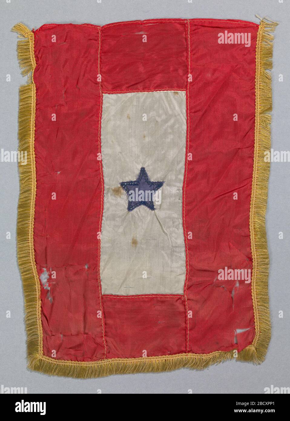 Bandiera a stella blu. La Bandiera della Stella Blu, o Bandiera di servizio, è un simbolo di un membro della famiglia in servizio militare. Il banner della bandiera di seta ha una stella blu al centro circondata da un campo rettangolare di bianco, inserito in un rettangolo rosso più grande. Una nappina d'oro circonda tre lati. Bandiera a stella blu Foto Stock