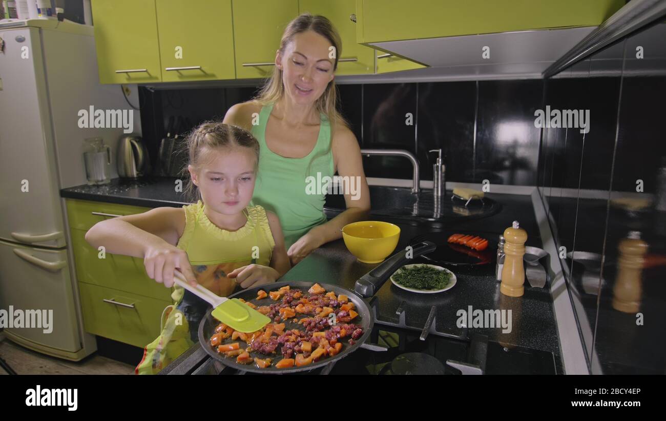 Madre che insegna figlia ragazza intelligente imparare a cucinare. Amante bambini per cucinare una frittata di uova napoletana fritte da salame affumicato salsiccia. Foto Stock