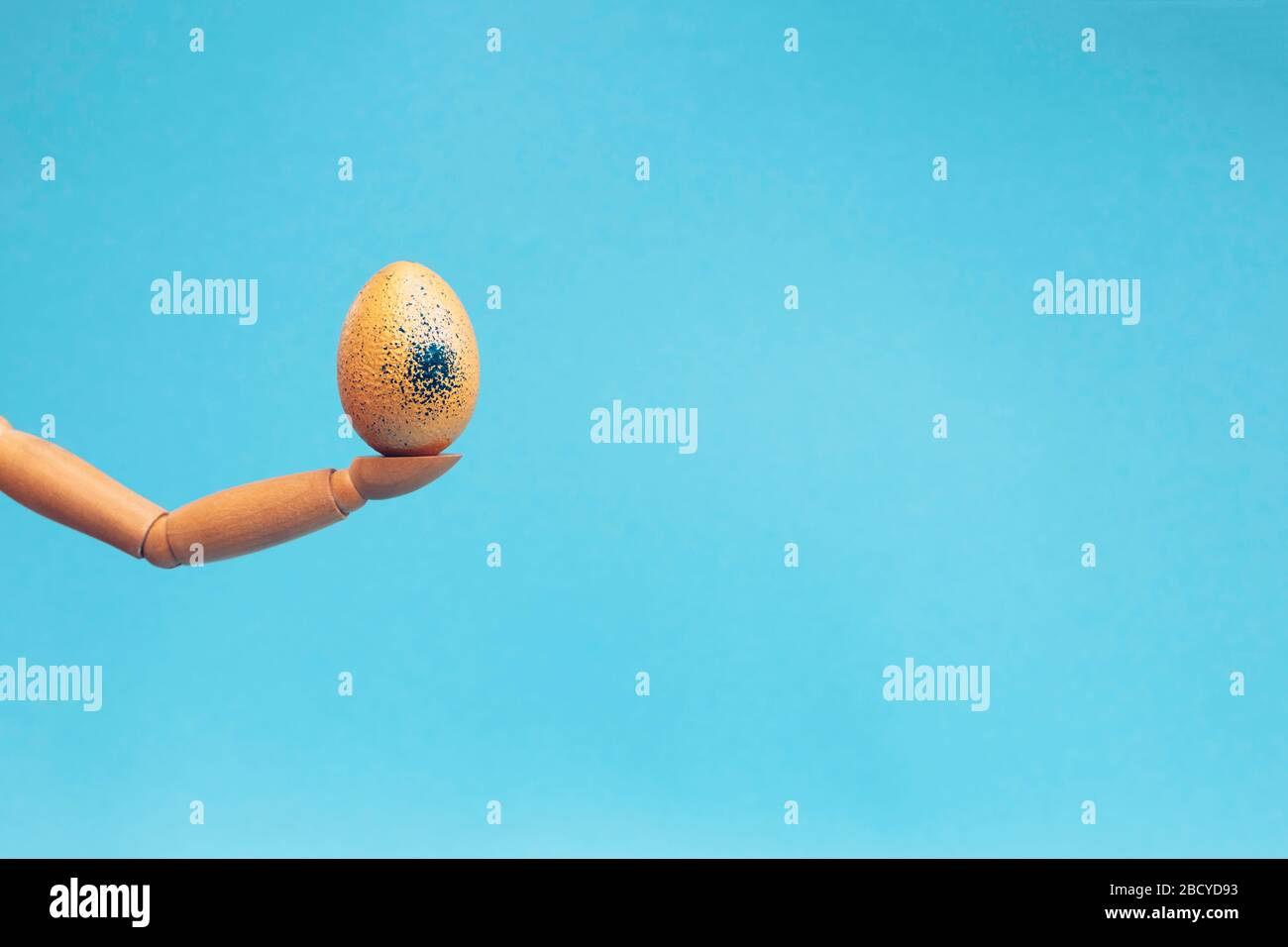 Mano di legno che tiene l'uovo dorato su sfondo blu. Posizionare per il testo. Concetto di Pasqua. Foto Stock