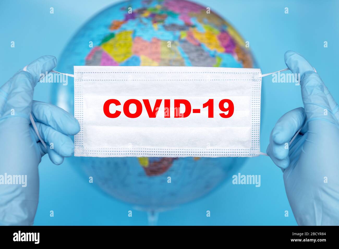 Maschera chirurgica protettiva per il viso in mano su un modello terrestre a globo. Concetto di coronavirus (covid-19) Foto Stock