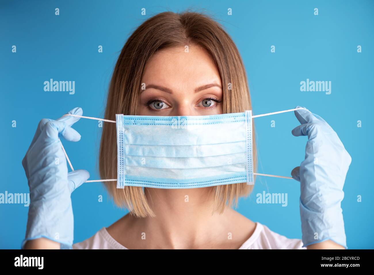 Il medico o l'infermiere che tiene in mano con la maschera facciale closeup del guanto su sfondo blu. Concetto sanitario e medico per prevenire la diffusione del virus Foto Stock