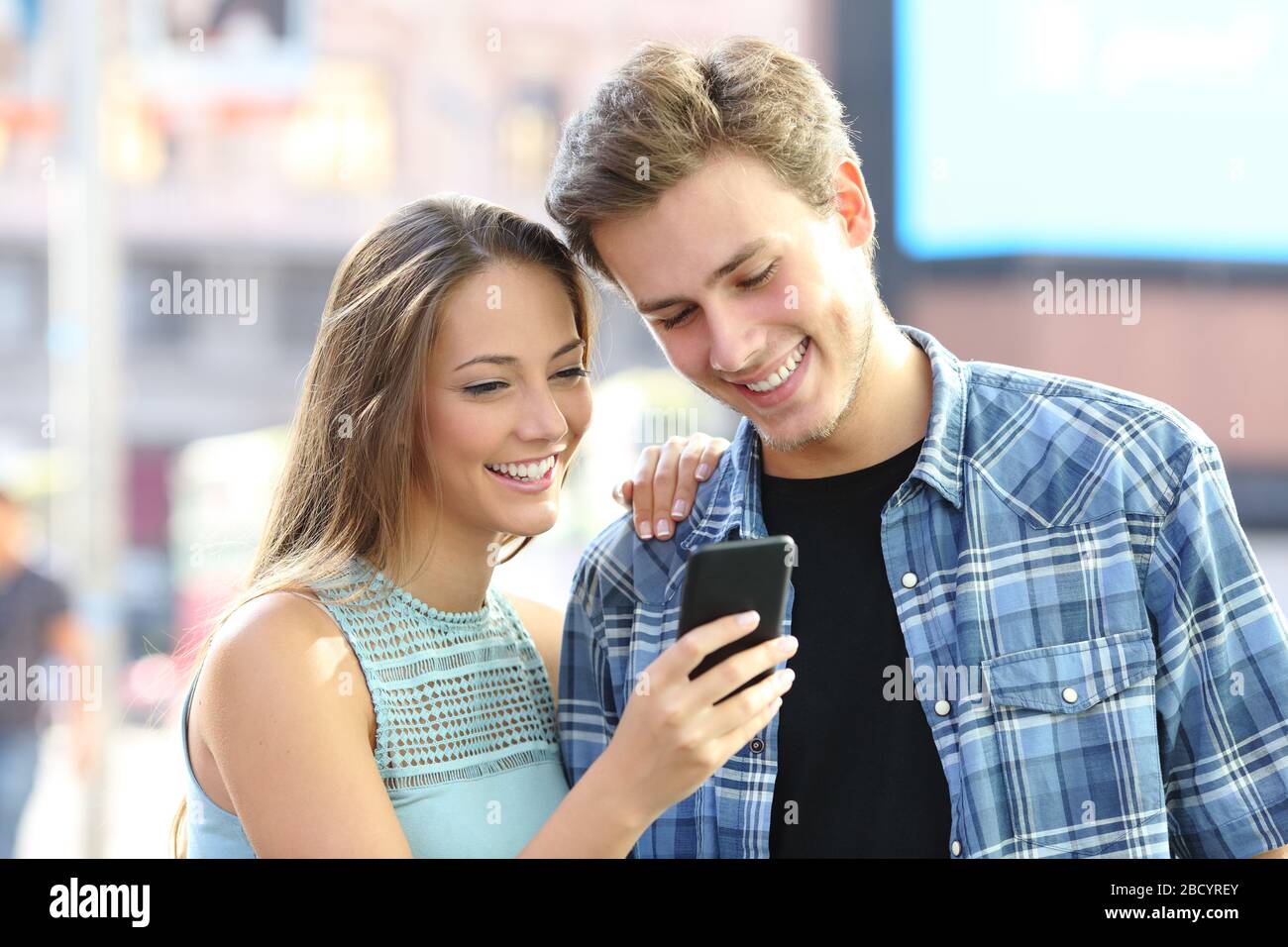 Felice giovane coppia leggere il contenuto sullo smartphone in piedi per strada Foto Stock