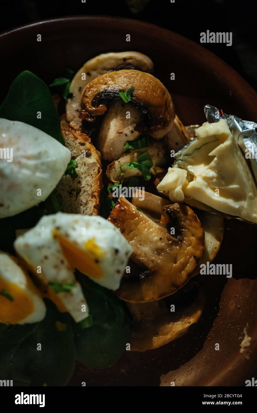Colazione appetitosa uova sode, toast, formaggio e funghi in un piatto di argilla su un fondo di legno. Uovo medio cotto. Foto Stock