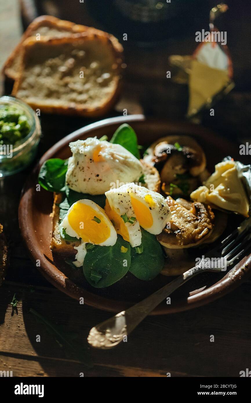 Colazione appetitosa uova sode, toast, formaggio e funghi in un piatto di argilla su un fondo di legno. Uovo medio cotto. Foto Stock