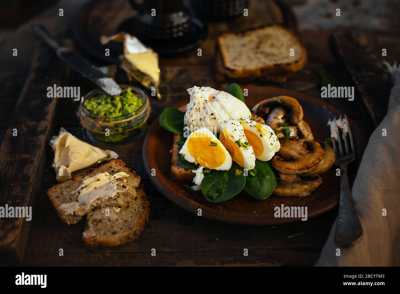 Colazione appetitosa uova sode, toast, formaggio e funghi in un piatto di argilla su un fondo di legno. Uovo medio cotto. Foto Stock