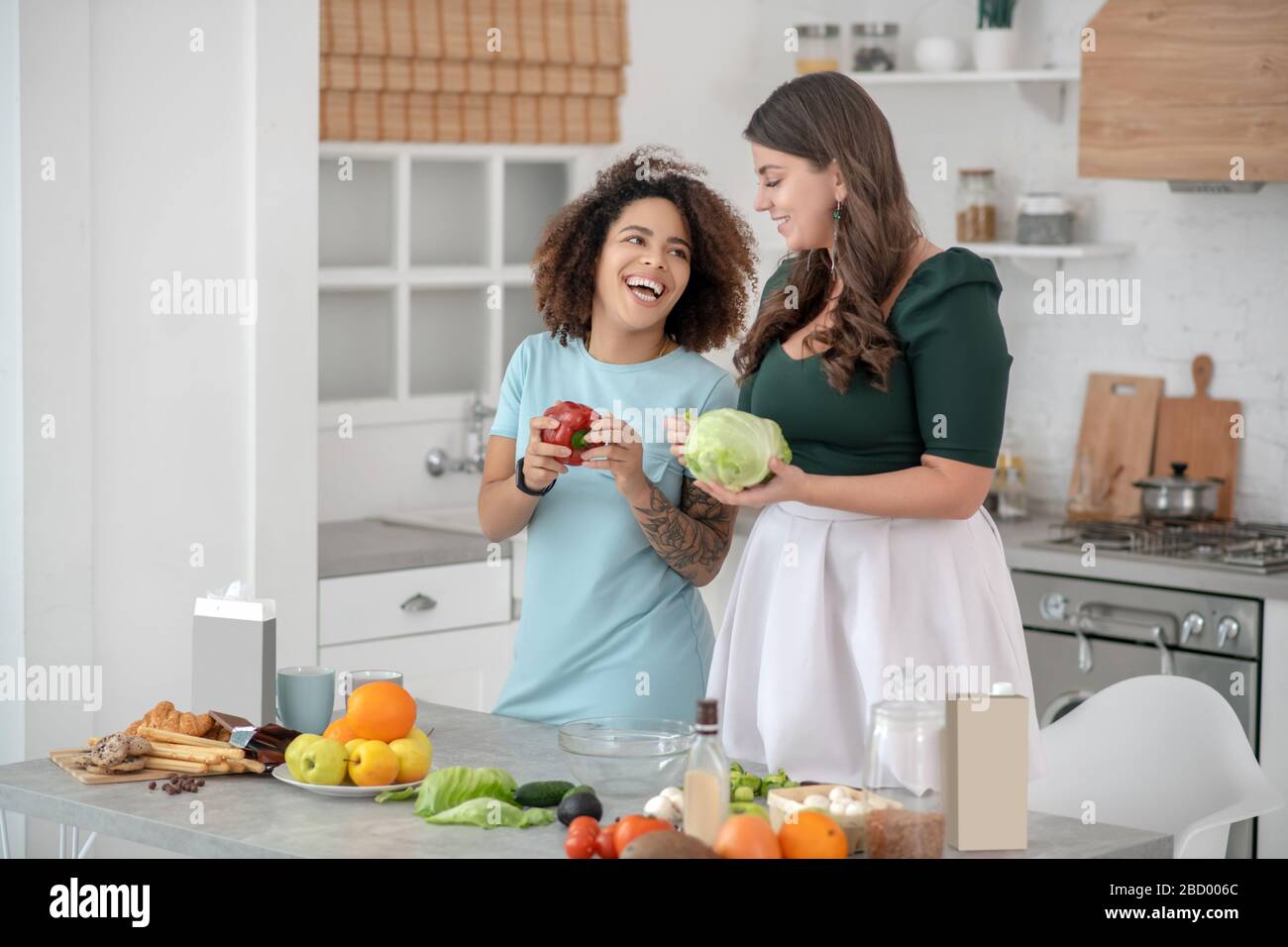 Due giovani donne con verdure in piedi in cucina. Foto Stock