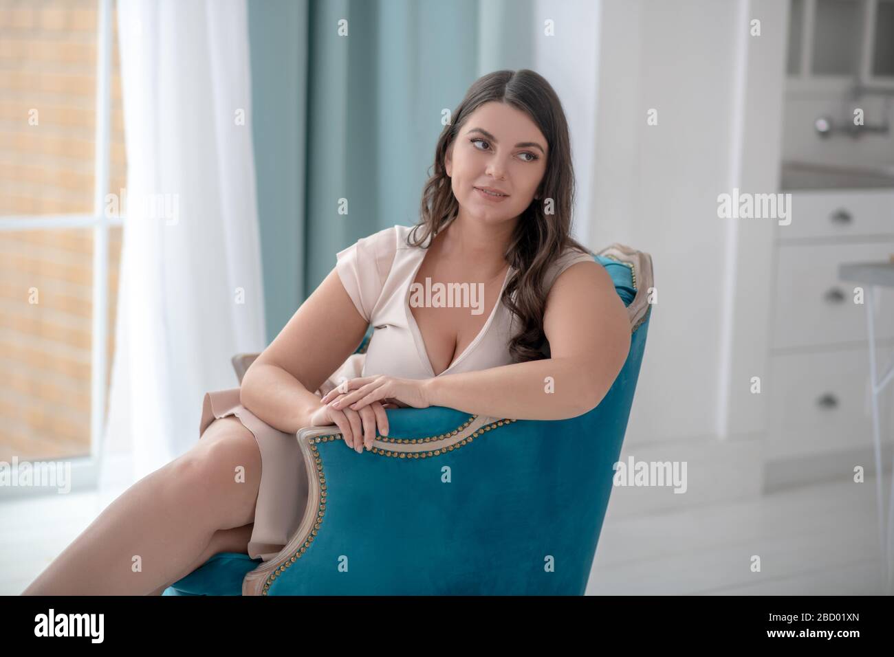 Donna dai capelli scuri seduta su una sedia in camera. Foto Stock