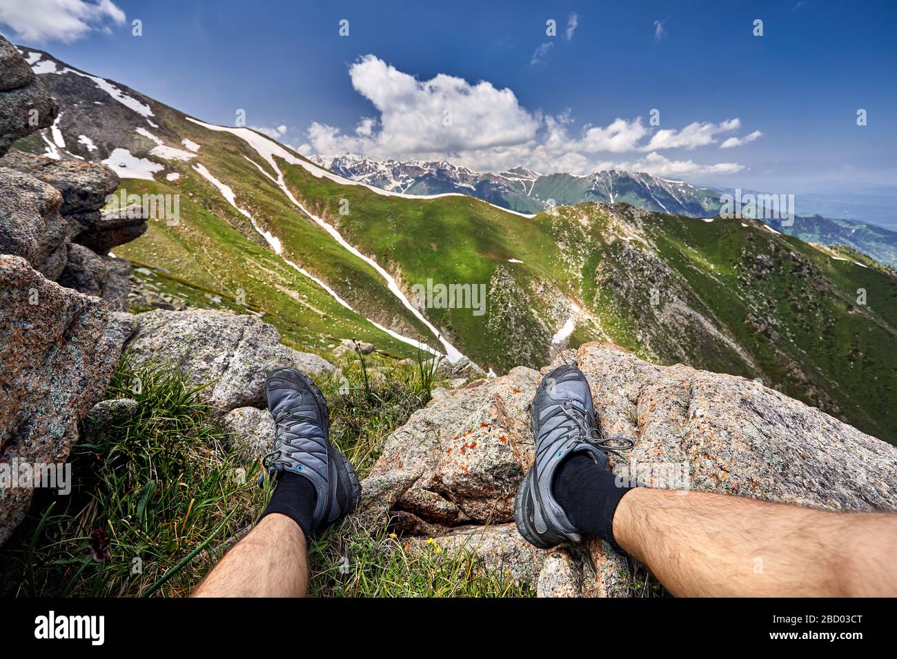 Gambe di uomo in scarpe di tracking e la vista delle montagne innevate con sfondo con cielo nuvoloso Foto Stock
