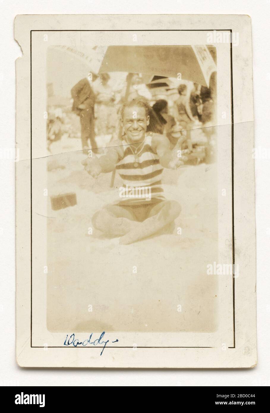 Fotografia di CPL Lawrence Leslie McVey sulla spiaggia. Una fotografia in bianco e nero di Lawrence McVey seduto su una spiaggia con le braccia distese alla macchina fotografica. McVey si siede con le gambe incrociate in una camicia scura e chiara spelata e shorts scuri. Proprio dietro McVey c'è un ombrellone. Fotografia di CPL Lawrence Leslie McVey sulla spiaggia Foto Stock