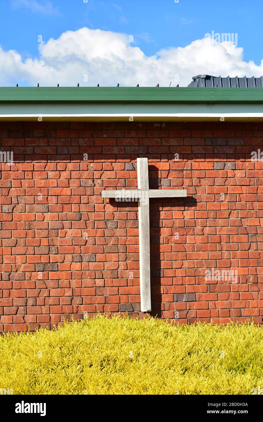 Croce cristiana in legno su pareti esterne in mattoni rossi di edificio chiesa contemporaneo. Foto Stock