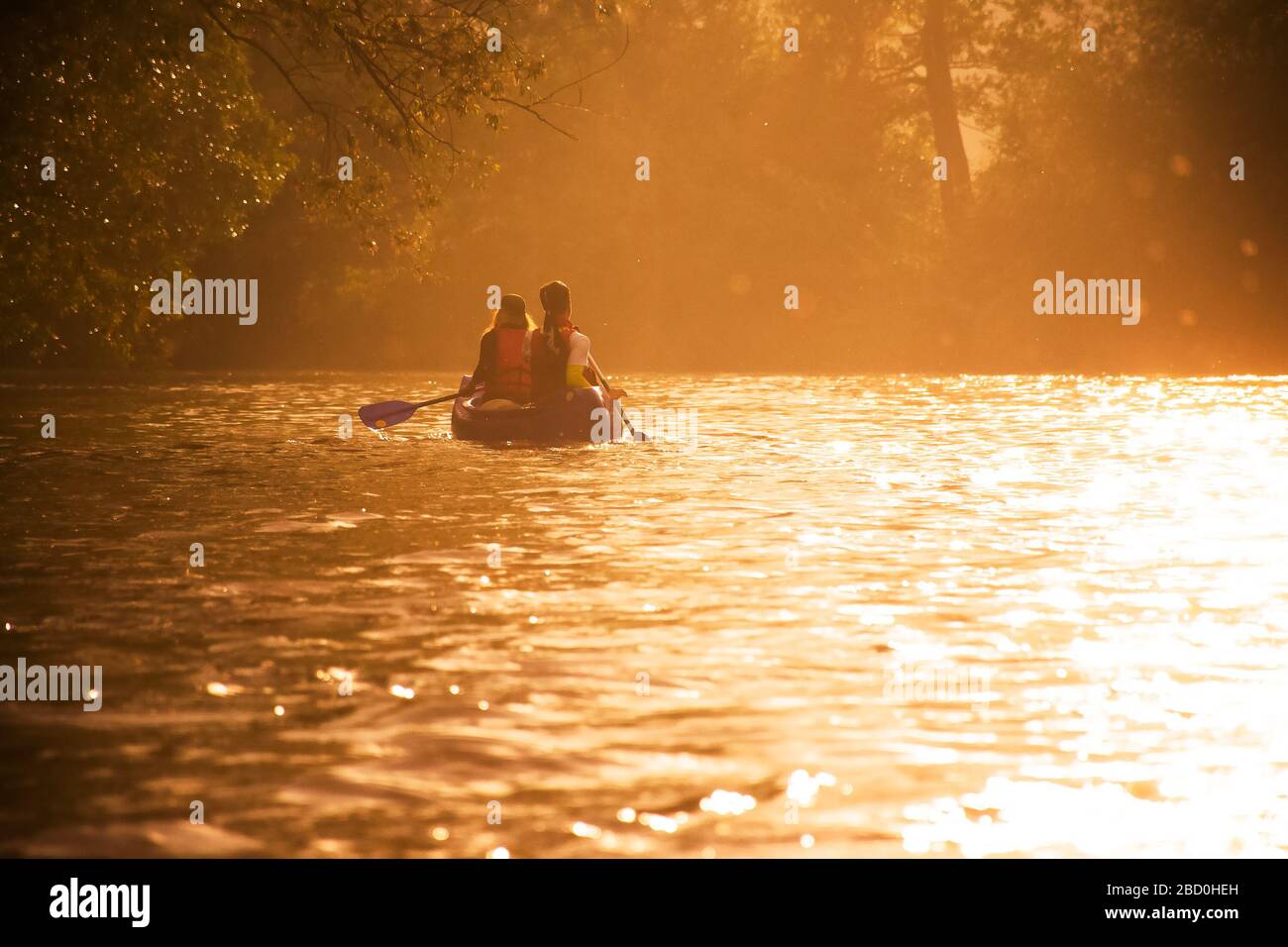 Due amici in canoa nuotano sul fiume con la bella luce dell'ultima sera Foto Stock