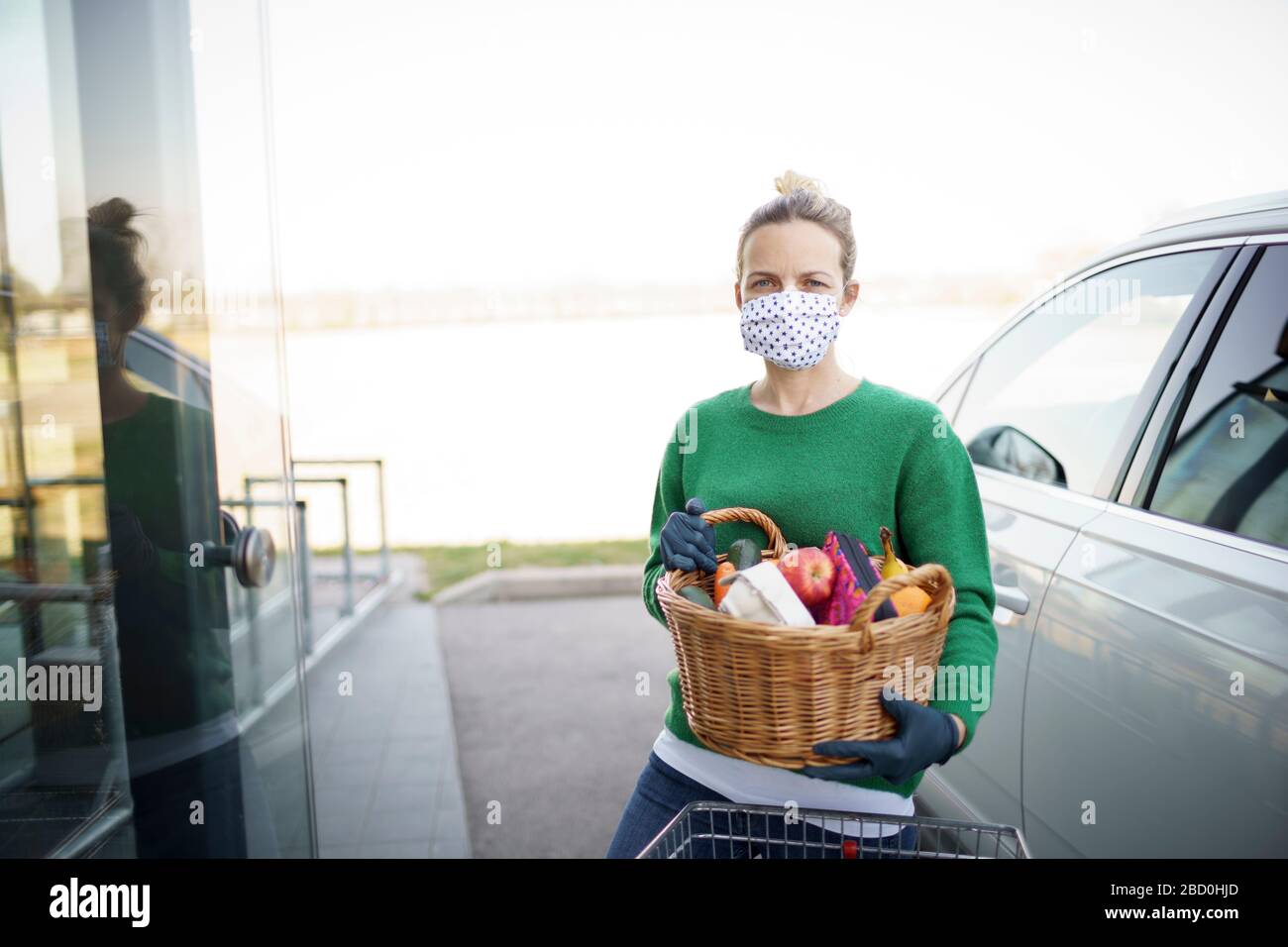 bella giovane donna è shopping con maschera di protezione della bocca durante la crisi corona covid e sta tenendo il suo carrello Foto Stock