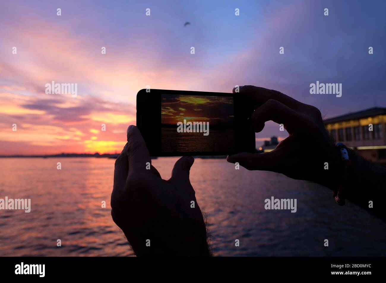 Le mani dell'uomo scattano foto con uno smartphone sulla costa di Istanbul, Kadikoy all'ora del tramonto. Foto Stock