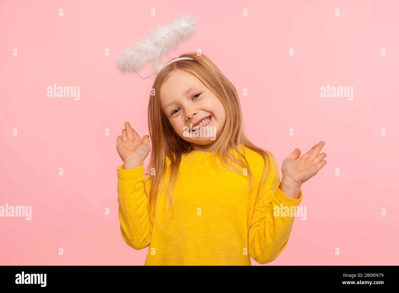 Giocosa bambina angelica che alza le braccia e guarda la macchina fotografica con il sorriso toothy, gesturing oops, non so, non ero io, bambino gioioso che nega la gui Foto Stock