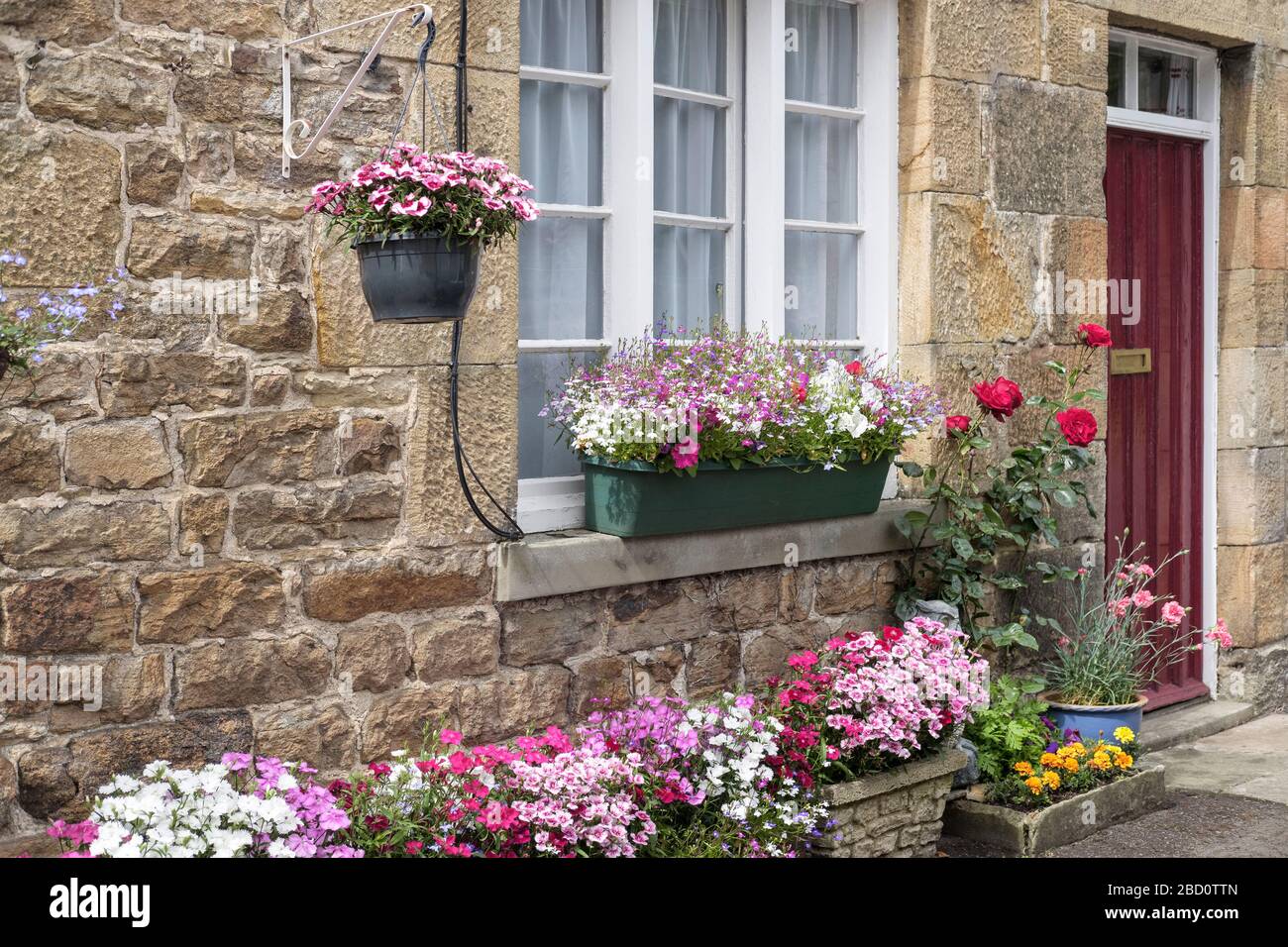 Vecchio portone cottage con cesti di fiori assortiti Foto Stock