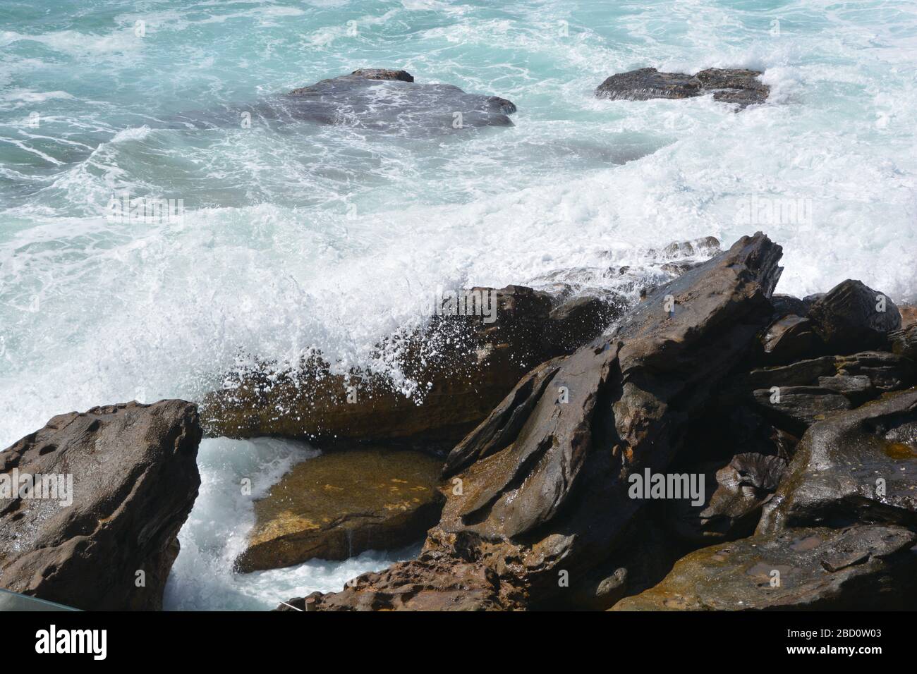 Vista ravvicinata delle onde che si infrangono sulle rocce a Bondi Beach, Australia; acqua blu e bianca dalla forza dell'acqua Foto Stock