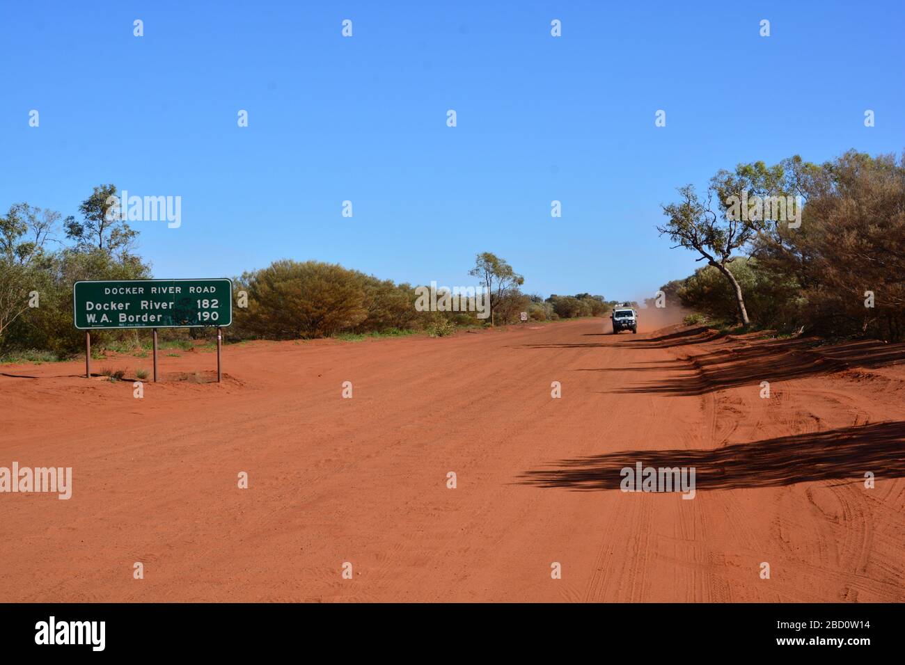 Ampio angolo di visuale della strada della polvere rossa con auto a trazione integrale che getta polvere rossa nell'entroterra del territorio del Nord, Australia; segnali stradali che indicano d Foto Stock