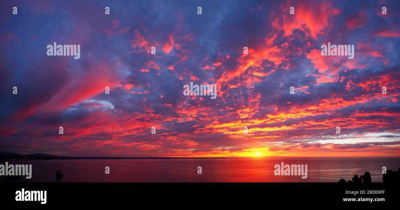 Splendida alba panoramica sull'oceano con splendide nuvole rosse e colori blu e viola Foto Stock