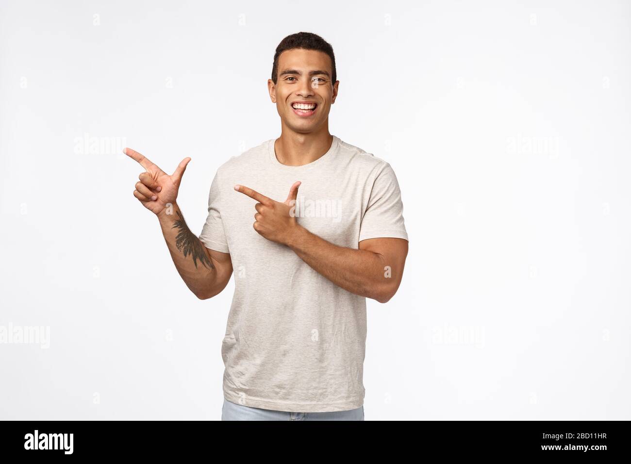 Allegro bello muscline uomo con tatuaggio sul braccio, tan, indossa una t-shirt bianco, rivolta a sinistra e sorridendo felice della fotocamera, introdurre il prodotto o promo Foto Stock