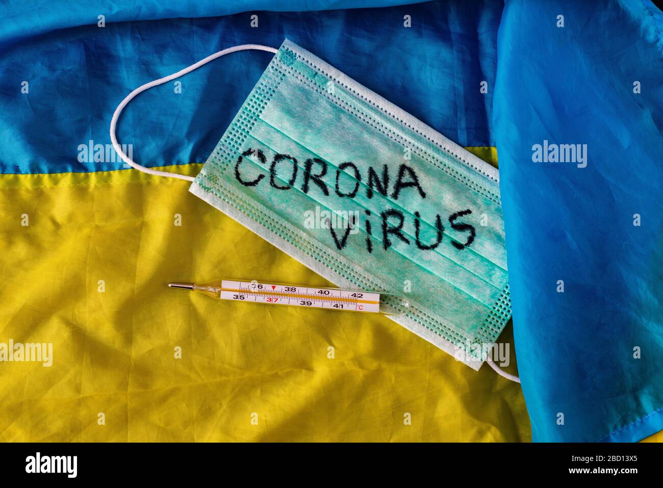 Concetto di coronavirus. Vista dall'alto di una maschera protettiva, termometro sulla bandiera dell'Ucraina. Nuova epidemia pandemica Foto Stock