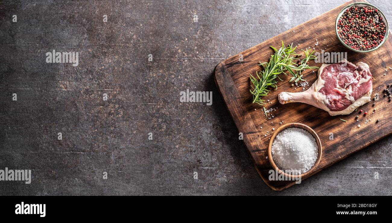 Top of view rustico tagliere in legno con coscia d'anatra, erbe, spezie e sale, che copre metà dello sfondo metalico. Foto Stock