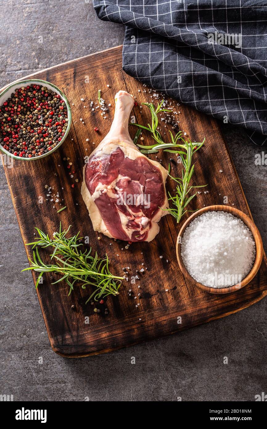 Formato verticale vista dall'alto di una gamba d'anatra su un asse di legno e sfondo metallico, circondato da tovaglia e ingredienti di stagione. Foto Stock