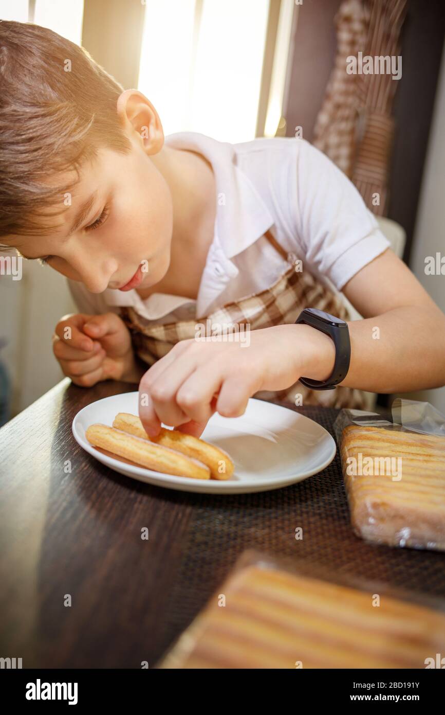 Ragazzo in grembiule disimballare biscotti savoiardi biscotto preparare il dessert tiramisù. Rimanete a casa e cucinate il cibo di sottofondo Foto Stock