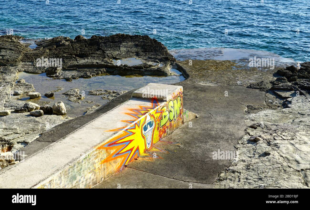 Pula, Croazia, 2 aprile 2020. Grafite colorata su un molo in pietra sulla spiaggia di pietra di fronte all'ingresso del mare azzurro Foto Stock