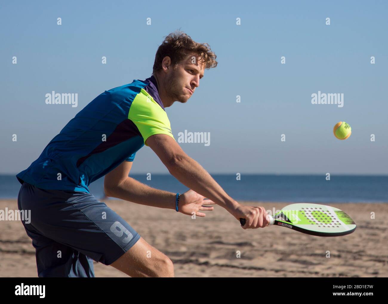 Un uomo in azione come lui gioca Beach Tennis con un sole cielo blu. Foto Stock