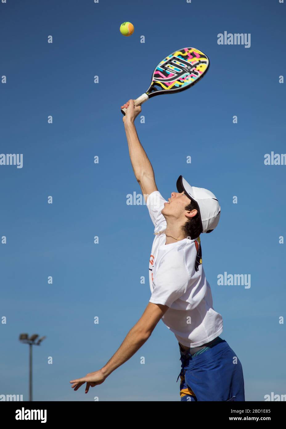 Un uomo in azione come lui gioca Beach Tennis con un sole cielo blu. Foto Stock